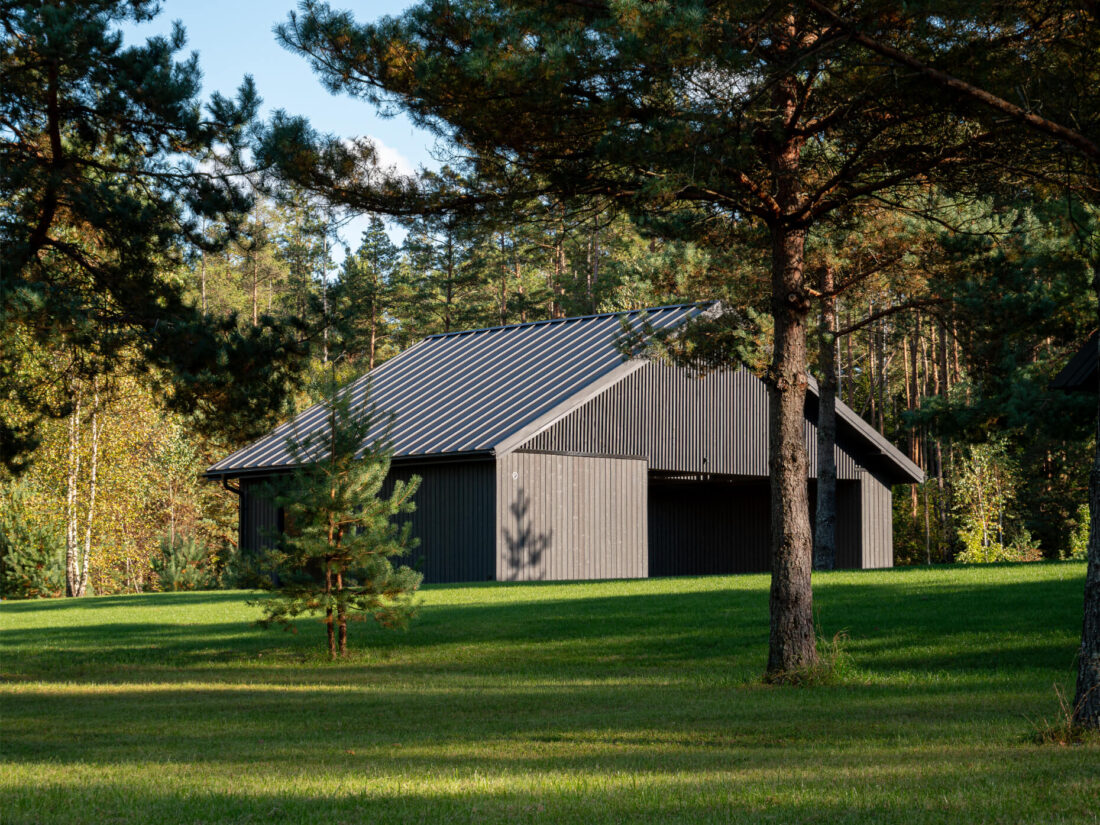 Exterior view of a modern gabled residence in Senieji Trakai featuring vertical Degmeda "Dark Grey" spruce charred wood cladding. The textured Shou Sugi Ban boards are paired with a dark metal standing seam roof and set within a forested landscape.