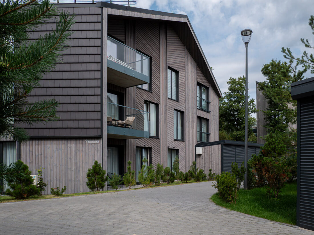Exterior view of a modern multi-apartment building in Palanga featuring Degmeda "Light Grey" spruce charred wood cladding installed in vertical and diagonal patterns. The brushed timber grain is paired with glass balconies and dark architectural tile siding.