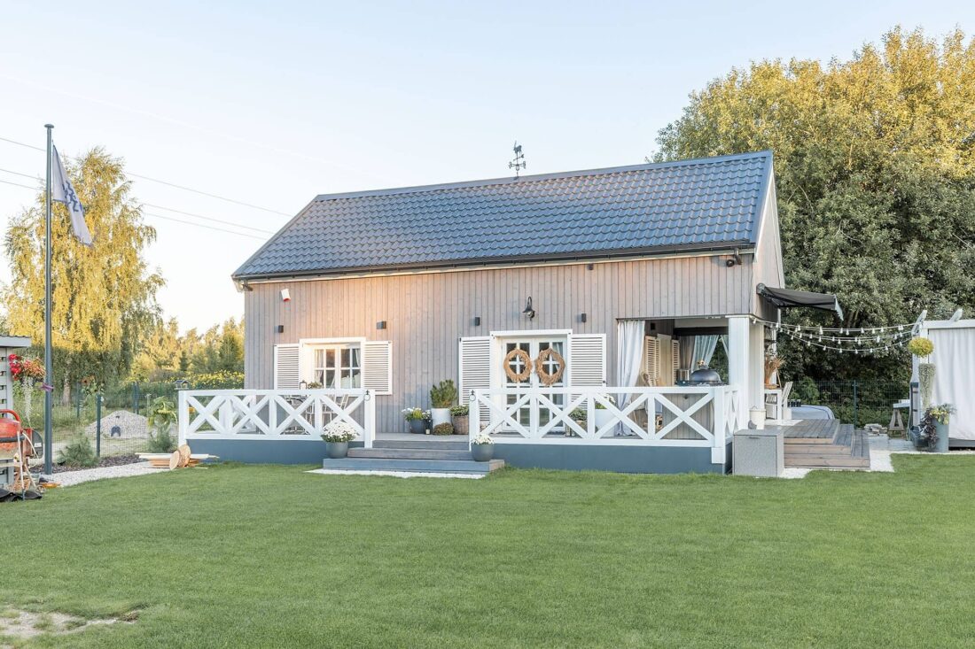 Exterior view of a traditional-style summer family house featuring vertical Degmeda "Light Grey" spruce charred wood cladding, accented with white terrace railings and window shutters.
