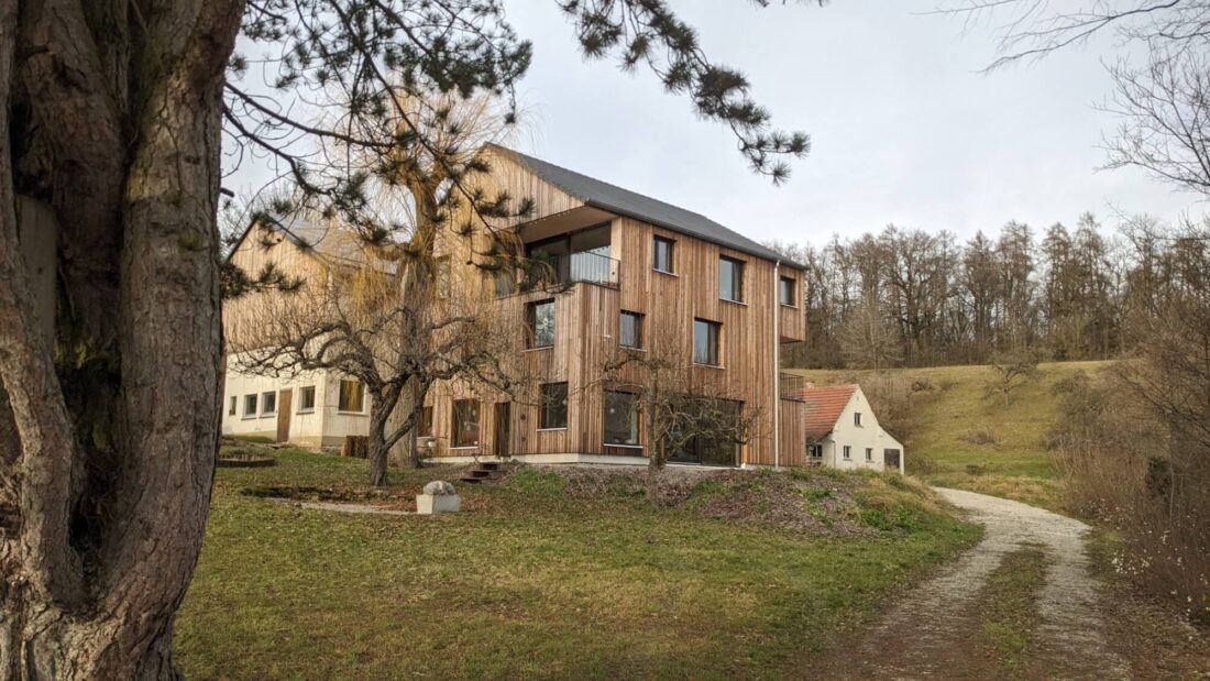 Exterior view of a modern residential building featuring vertical C-class Degmeda "Natural" brushed charred larch wood cladding, harmonizing with the surrounding nature and landscape.