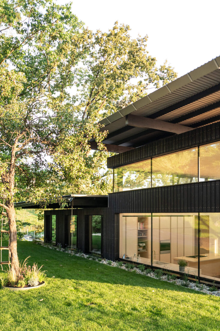 Facade detail of the House Above the City project in Slovenia, showcasing vertical Degmeda "Dark Black" larch charred wood boards integrated with large-scale glazing and exposed structural timber beams.