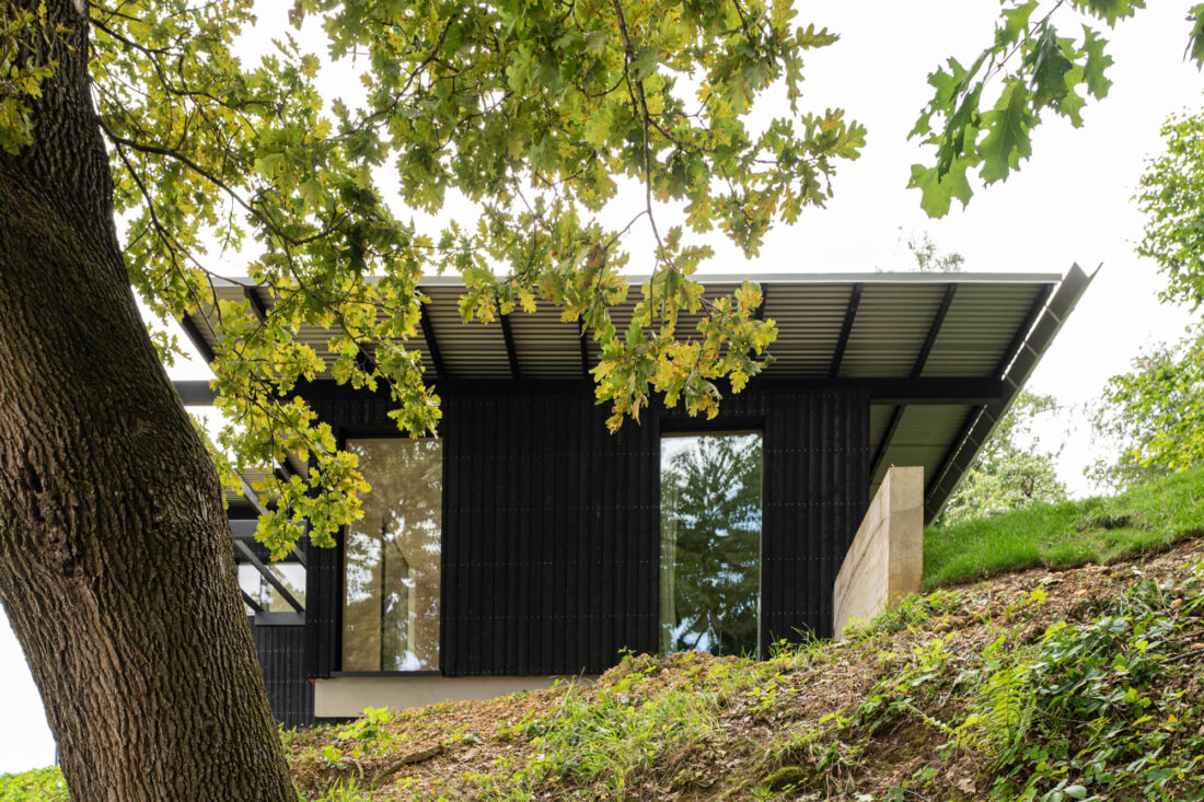 Hillside elevation of the House Above the City project in Slovenia, showcasing vertical Degmeda "Dark Black" larch charred wood boards under a wide roof overhang.