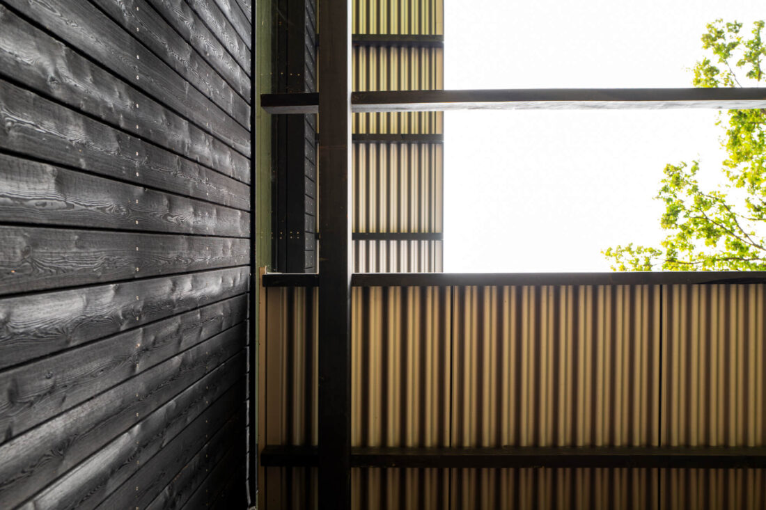 Close-up detail of horizontal Degmeda "Dark Black" larch charred wood boards showing the expressive grain texture next to a translucent screen in the House Above the City project, Slovenia.