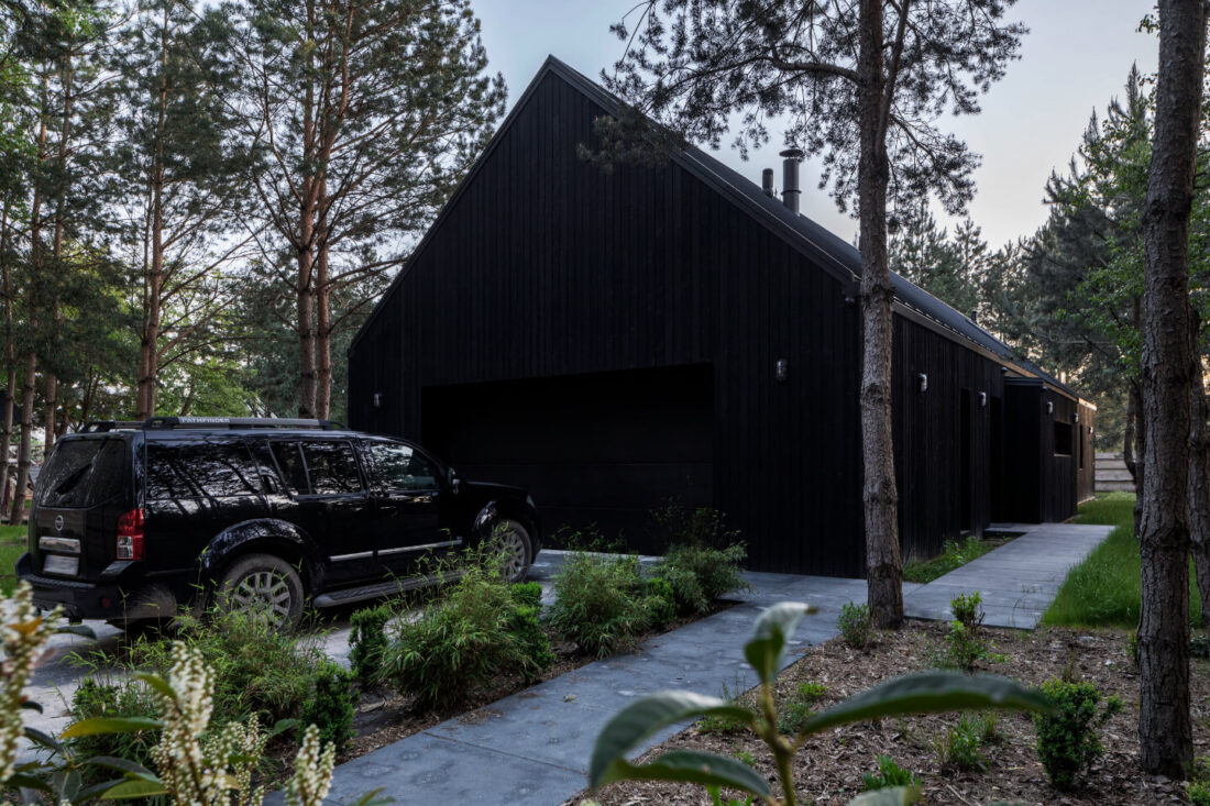 Side view of a modern forest home in Poland featuring a gabled facade with vertical Degmeda "Dark Black" larch charred wood cladding and an integrated garage.