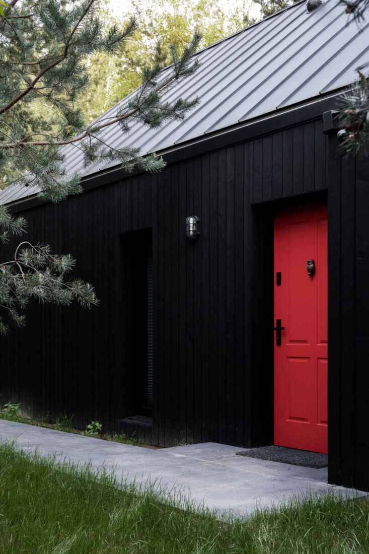Close-up of a modern home entrance in Poland featuring vertical Degmeda "Dark Black" larch charred wood cladding contrasted by a vibrant red front door.