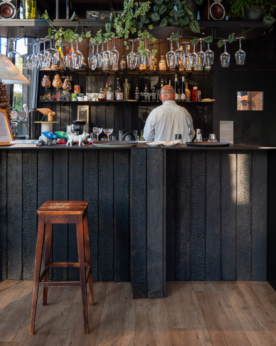 Interior of Velo Bar in Lithuania featuring a bar counter and back wall finished with Degmeda "Deep Char" larch charred wood boards.