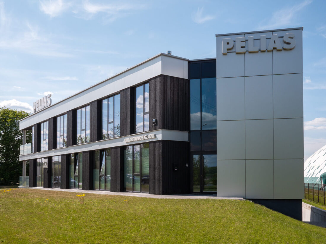 Exterior view of the Pelias office building in Kaunas, featuring vertical Degmeda Deep Char Spruce cladding installed between large glass windows, contrasted by sleek silver metal panels and corporate signage.