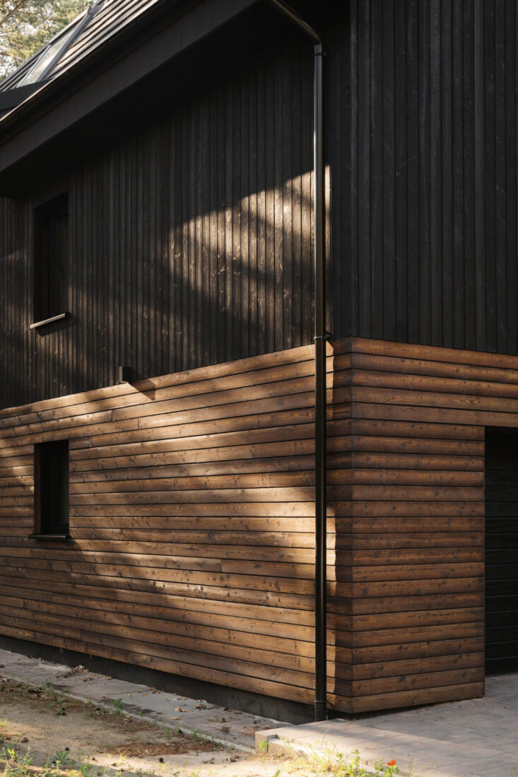 Close-up corner detail of the Wawer Barn in Poland featuring a contrast between vertical Degmeda "Dark Black" larch boards and horizontal "Amber" larch boards with sunlight shadows.
