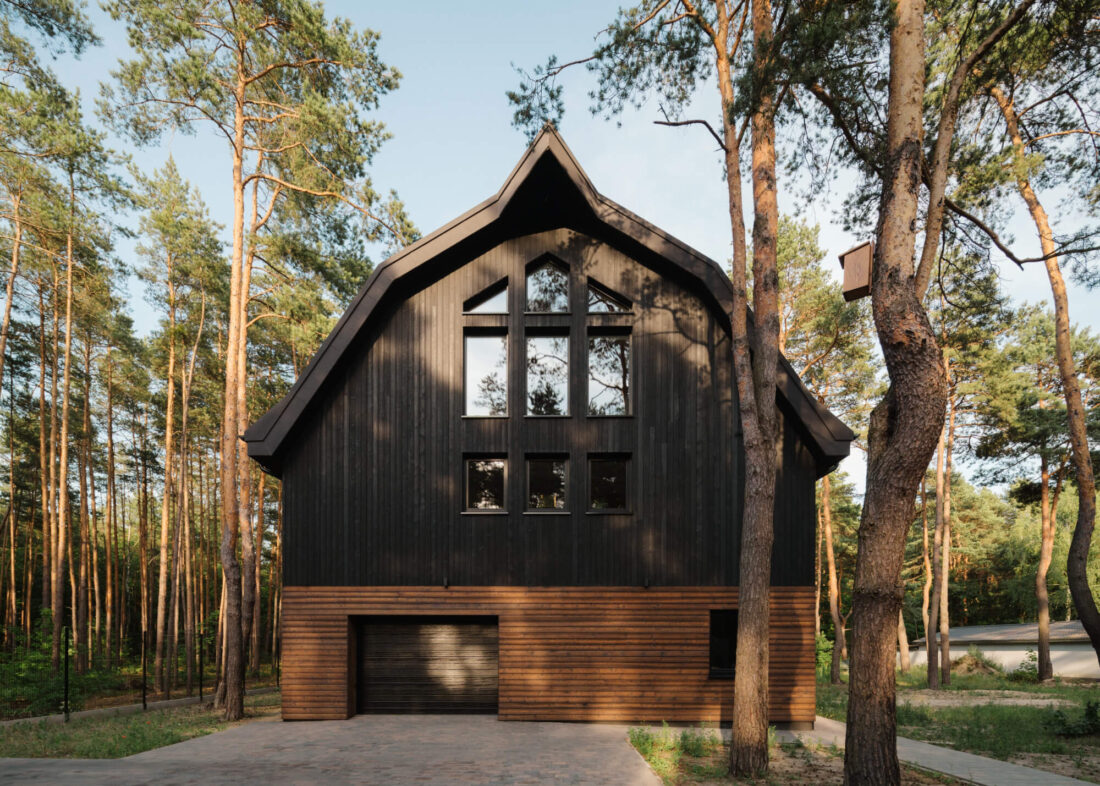 Symmetrical front view of the Wawer Barn residence in Poland featuring vertical Degmeda Dark Black larch boards on the gabled upper volume and horizontal Amber larch boards at the base.