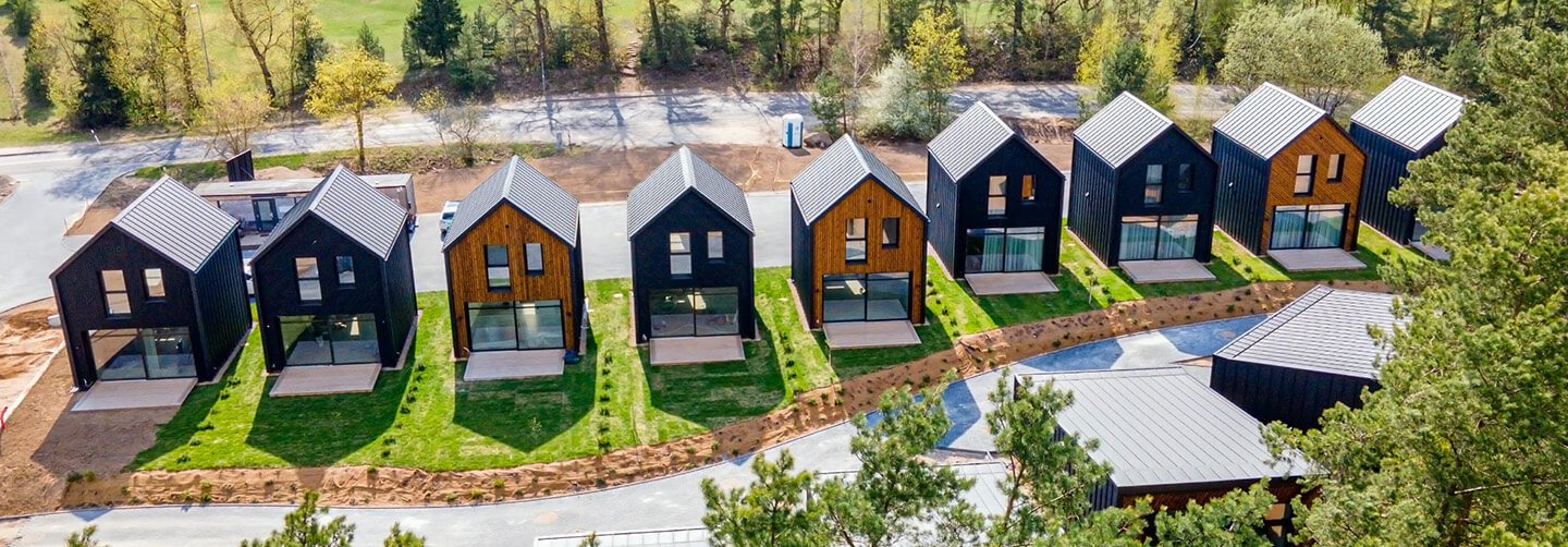 Aerial view of the Lake Villas development in Vilnius featuring a row of modern gabled houses clad in alternating Degmeda "Dark Black" and "Amber" spruce boards.
