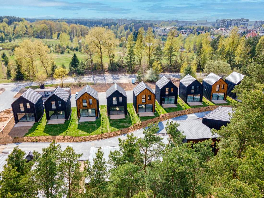 Aerial perspective of the Lake Villas residential project in Vilnius showcasing modern gabled houses clad in alternating vertical Degmeda "Dark Black" and "Amber" spruce boards set against a pine forest.