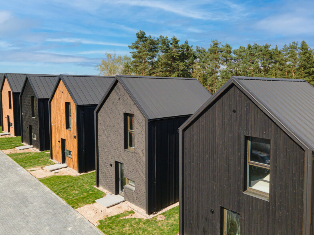 Elevated side view of the Lake Villas development in Vilnius showing a row of modern gabled houses clad in alternating vertical Degmeda Dark Black and Amber spruce boards.