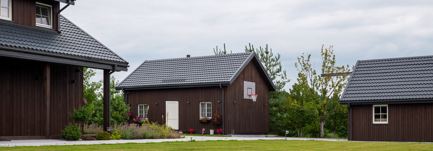 Exterior view of a residential complex in Lithuania featuring multiple buildings with vertical Degmeda Dark Brown larch boards and traditional grey tile roofs.