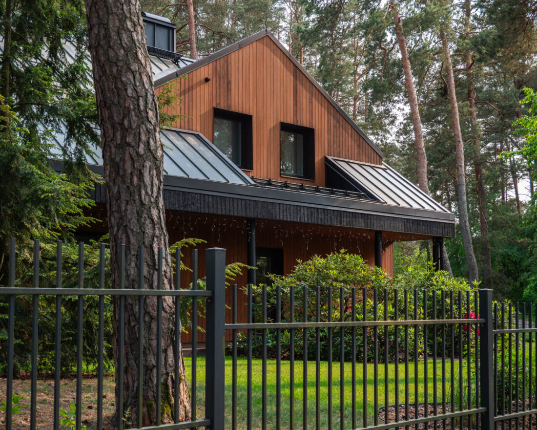Side view of the Forest Edge Residence in Kačerginė featuring vertical Degmeda "Amber" and "Deep Char" larch charred wood cladding under a dark metal roof.