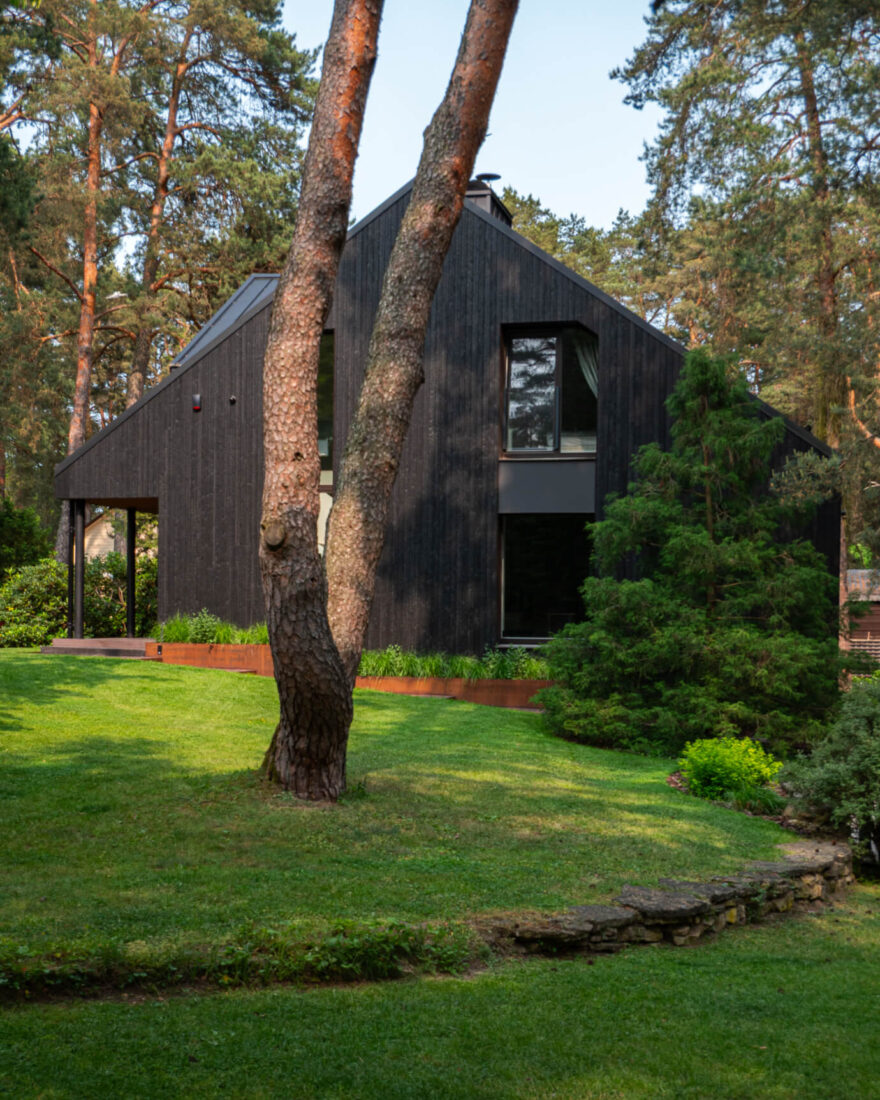 Exterior facade of the Forest Edge Residence in Kačerginė featuring vertical Degmeda Deep Char larch charred wood cladding and large windows overlooking a landscaped garden.