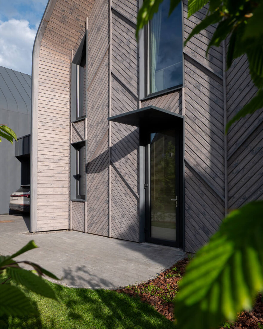 Entrance view of a modern residence in Kaunas featuring Degmeda "Light Grey" spruce facade boards in a chevron pattern and a dark metal door canopy.