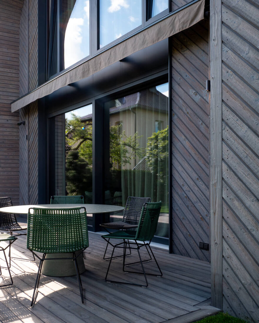 Exterior terrace view of a modern residence in Kaunas featuring Degmeda "Light Grey" spruce facade boards in a chevron pattern and an integrated wooden deck with outdoor furniture.