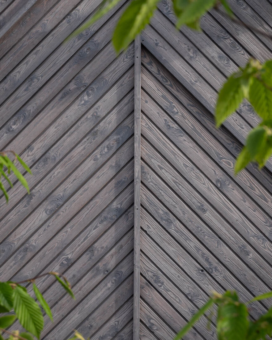 Macro detail of Degmeda "Light Grey" spruce charred wood boards installed in a decorative chevron pattern, highlighting the natural wood grain and precision jointing.