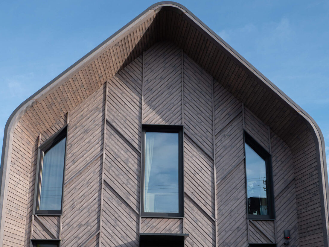 Detail view of the gabled facade on a modern residence in Kaunas, showcasing Degmeda "Light Grey" spruce facade boards installed in a precise chevron pattern.