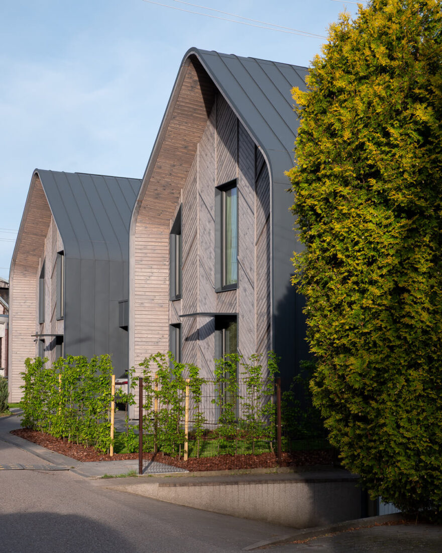 Street view of a modern residential building in Kaunas featuring a rhythmic chevron pattern of Degmeda "Light Grey" spruce charred wood boards and curved architectural metal roofing.