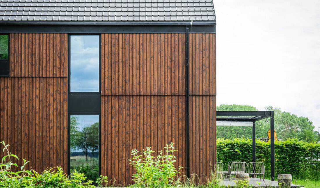 Detail of the facade at Glass Gable House in Poland, featuring vertical Degmeda "Red Amber" larch boards and large windows with dark architectural frames.