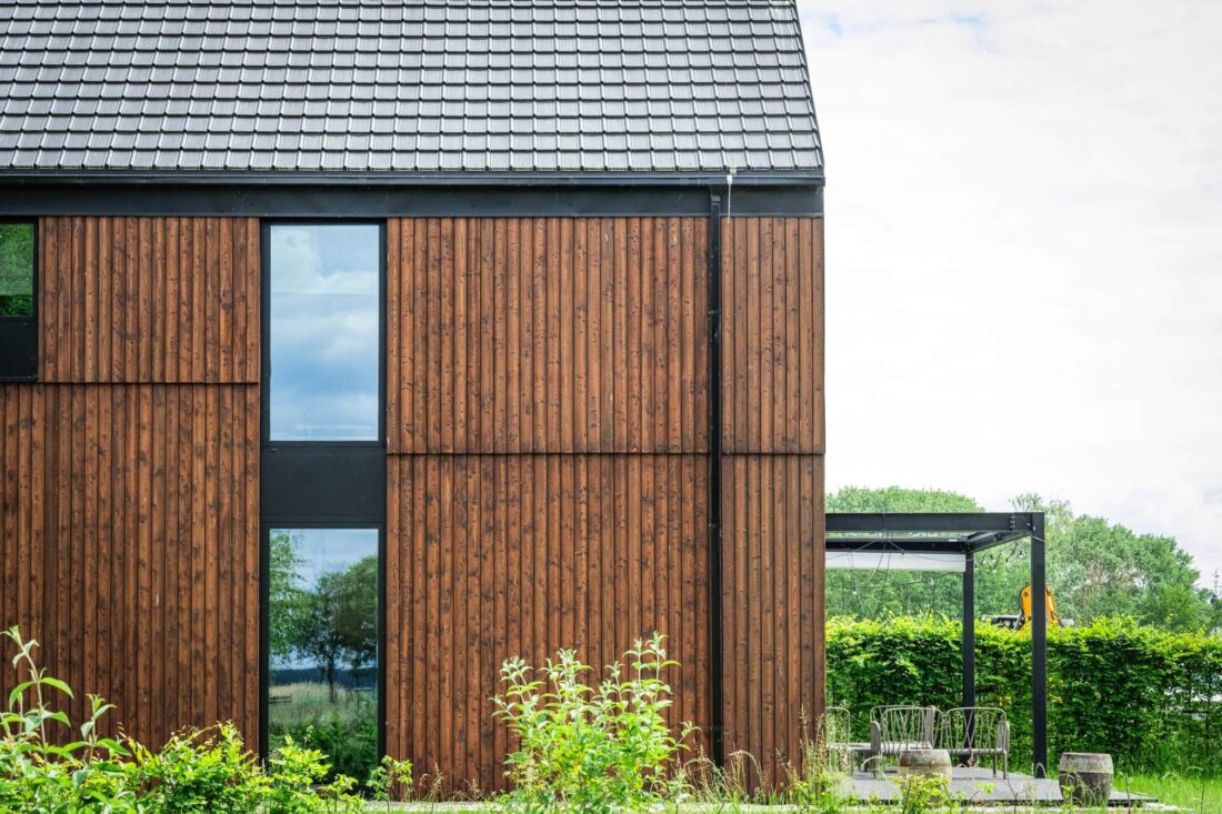Detailed elevation view of the Glass Gable House in Poland, featuring the rich grain and warm brown tone of vertical Degmeda "Red Amber" larch boards.