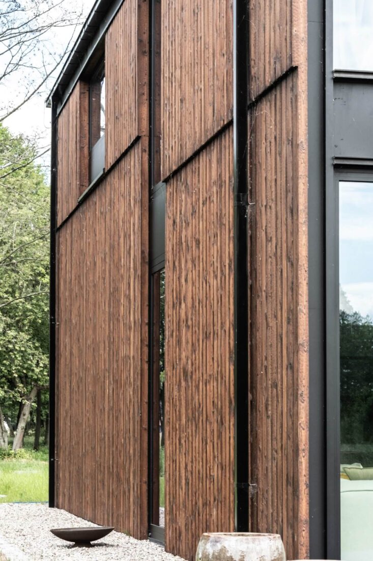 Side view of the Glass Gable House facade in Poland showing vertical Degmeda "Red Amber" larch boards with visible charred grain texture and dark architectural detailing.