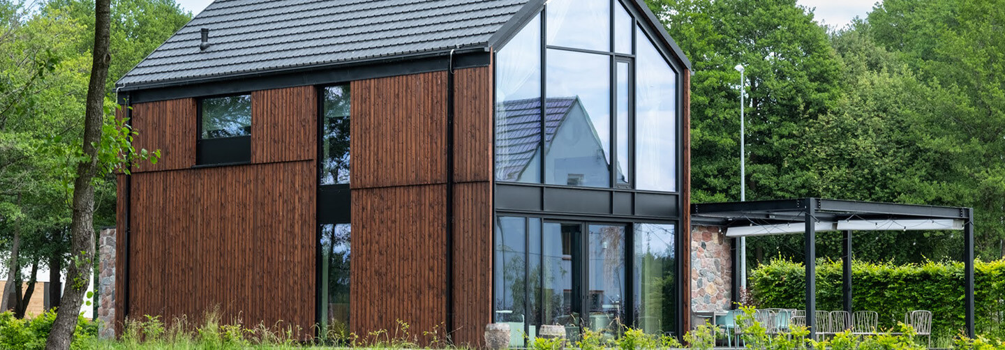 Exterior view of the Glass Gable House in Poland featuring vertical Degmeda "Red Amber" larch charred wood boards and a large glass gabled facade.
