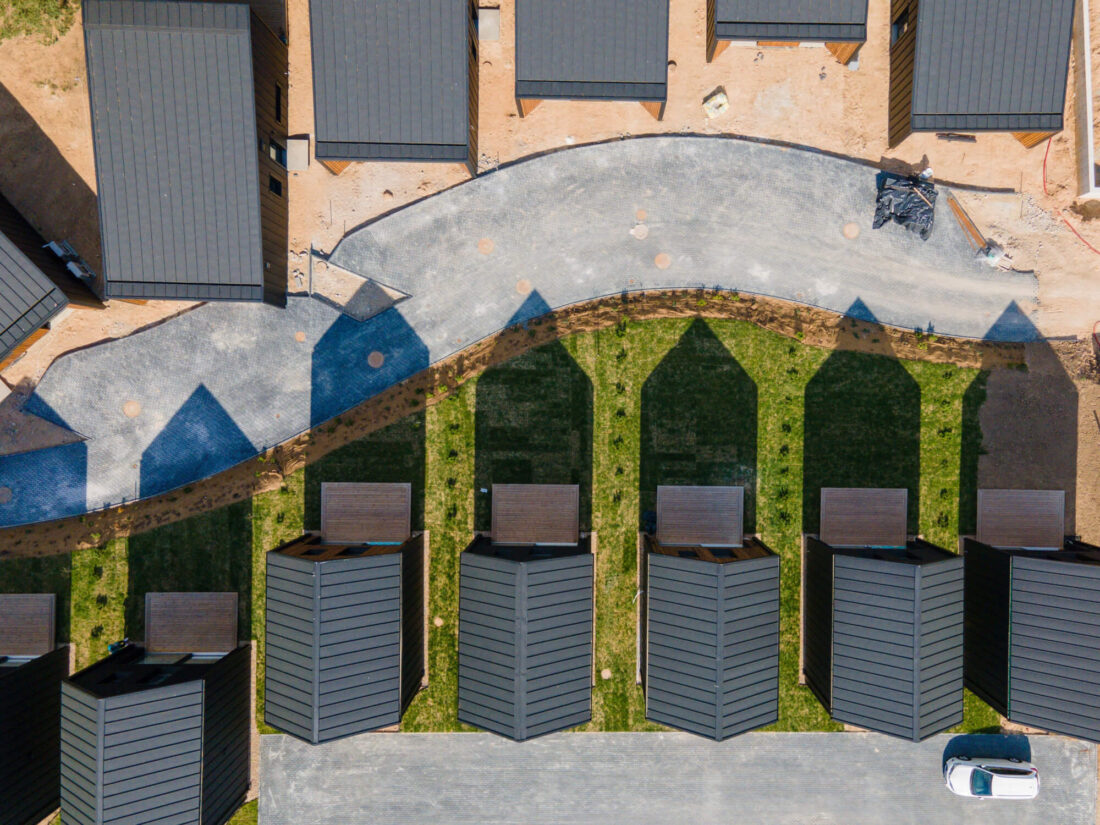 Top-down aerial view of the Lake Villas development in Vilnius, showcasing the rhythmic arrangement of gabled houses featuring Degmeda spruce facade boards and black standing seam roofs.