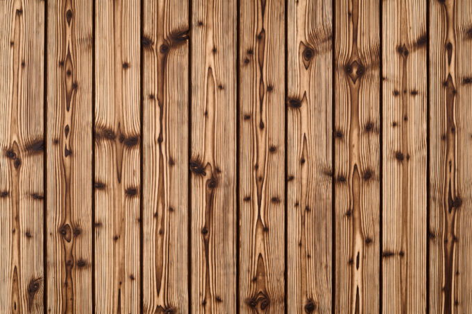Close-up of vertical wooden planks with natural grain and knots in warm brown tones, like a wooden wall or deck paneling.