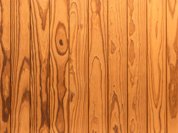 Termo-Pinus-Radiata-brushed Close-up of vertical wooden planks with natural grain and a warm orange-brown finish, resembling a wooden wall or paneling.